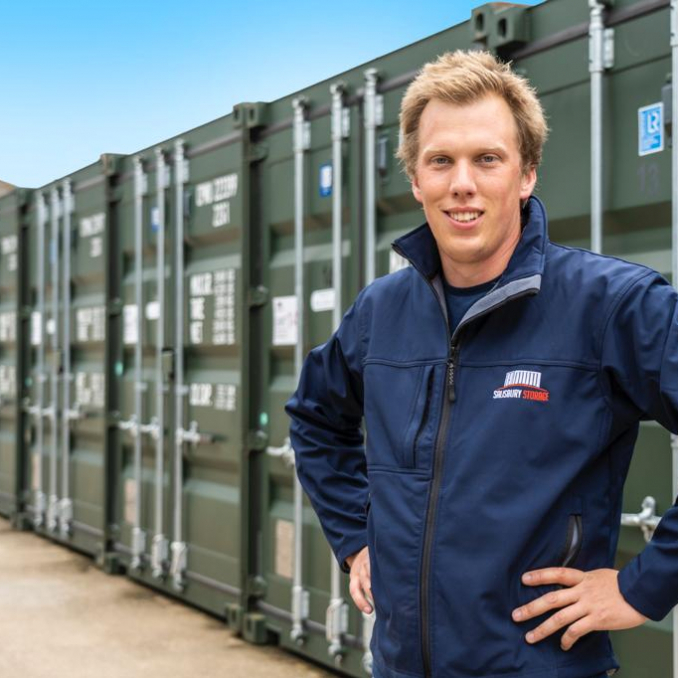 Man stands smiling with hands on hips in front of green storage container